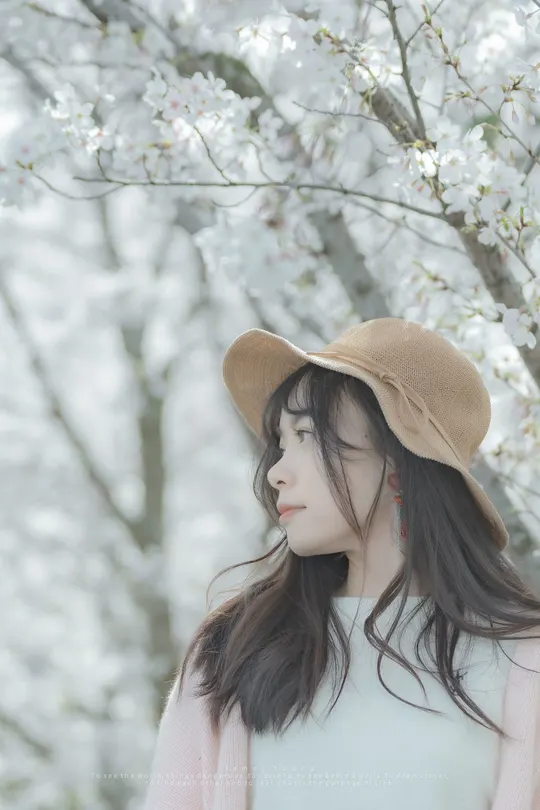 一位美丽的年轻女子戴着帽子站在盛开的花树前