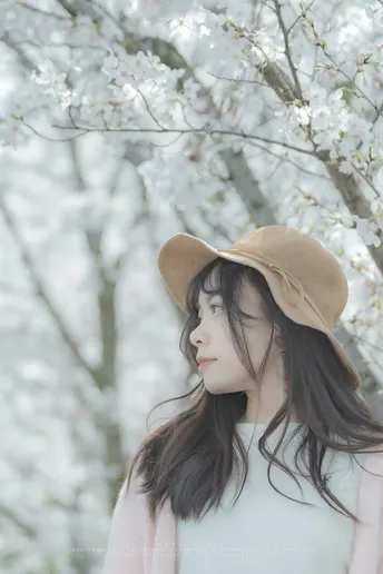 一位美丽的年轻女子戴着帽子站在盛开的花树前