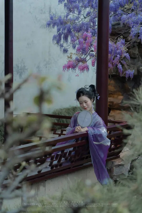 一位穿着和服的年轻女子站在一座有紫花建筑前