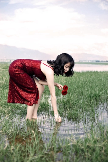 一个穿着红色连衣裙的年轻女子在被洪水淹没的田地里摘花