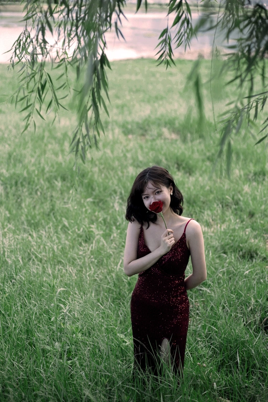 一个穿着红色连衣裙的年轻女子站在高高的草地上 手里拿着一朵花
