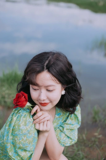 一个年轻的女人坐在湖边 手里拿着一朵红花 还有一个小女孩坐在水边
