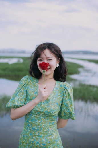 一位身穿绿色连衣裙的年轻女子站在被洪水淹没的田地里 脸前放着一朵红玫瑰