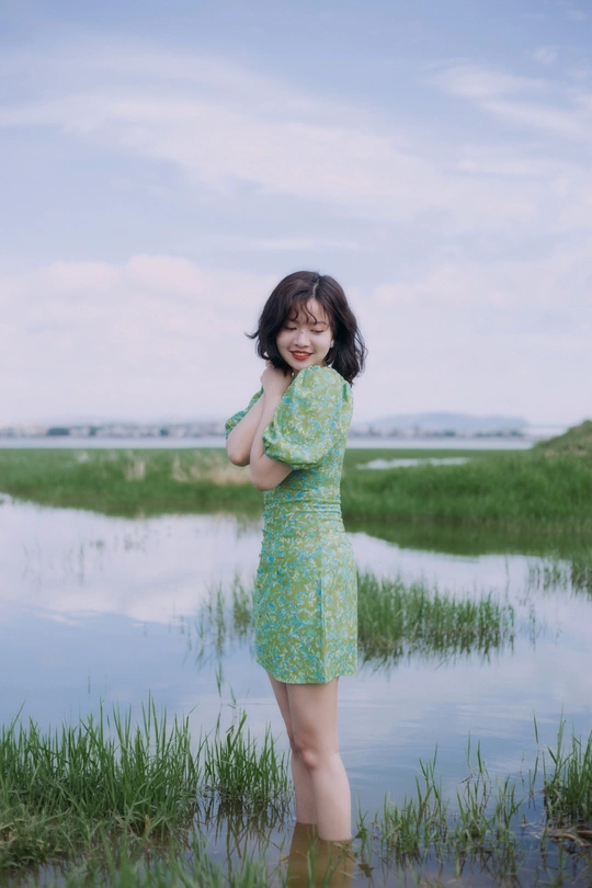 一个穿着绿色连衣裙的年轻女子站在一个小湖旁的沼泽地里
