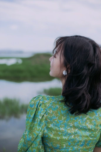 一个穿着绿色连衣裙的年轻女子望着水面