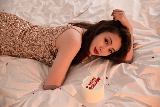 一个穿着白色连衣裙的年轻女子躺在床上 手里拿着一杯东西。