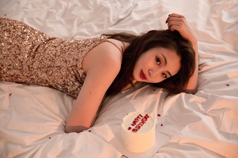 一个穿着白色连衣裙的年轻女子躺在床上 手里拿着一杯东西。