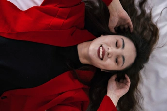 一位穿着红衬衫和红外套的年轻女子躺在床上 头发散开 带着微笑。