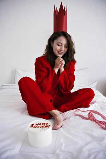 一位穿着红色衣服的女人坐在床上 桌子上放着一个蛋糕。