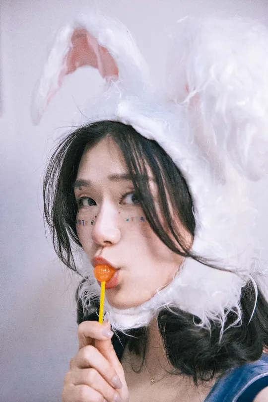 一位戴着兔子耳朵帽子的年轻女子 口中咬着一根胡萝卜 身着脸上带着兔子耳朵的服装。