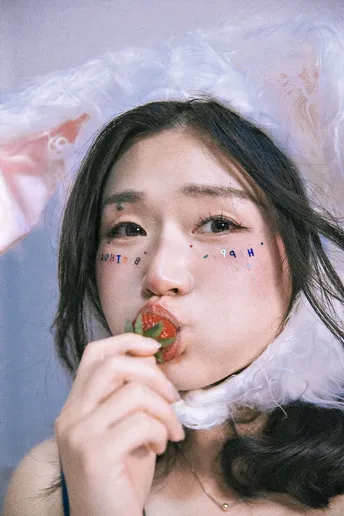 一位年轻女子穿着服装 脸上化了妆 正在吃草莓。