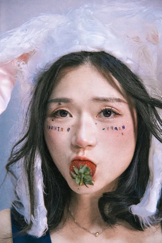 一位涂着口红的女孩 嘴里含着草莓。