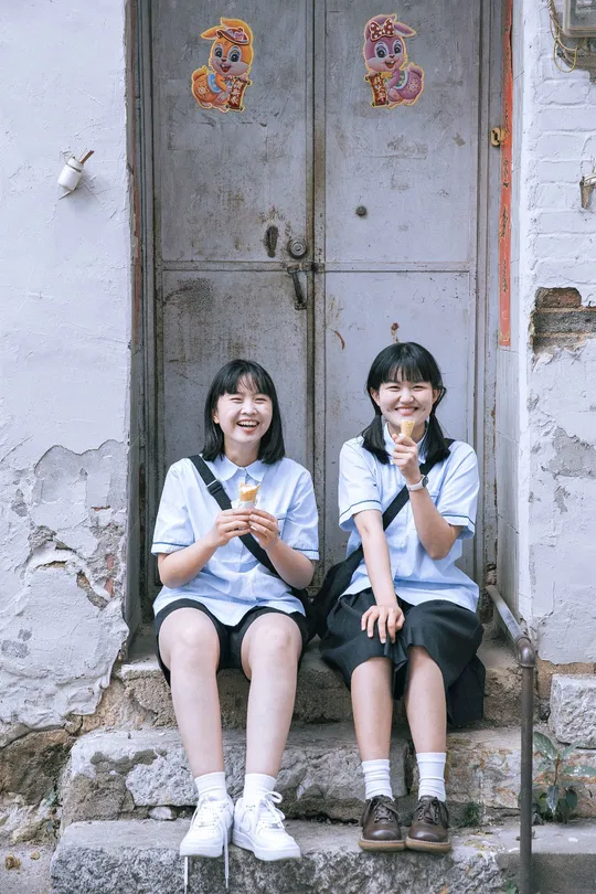 两个穿校服的女孩坐在建筑物外的台阶上