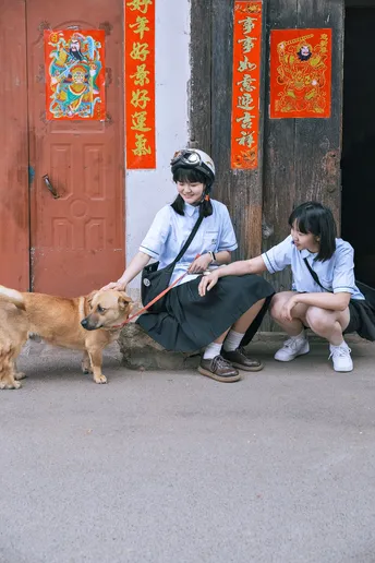 一个妇女和一个小女孩坐在建筑物外面 狗在绳子上。