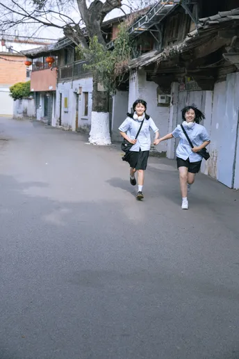 一些穿着制服的年轻人跑过一座破败的建筑物前面的街道。