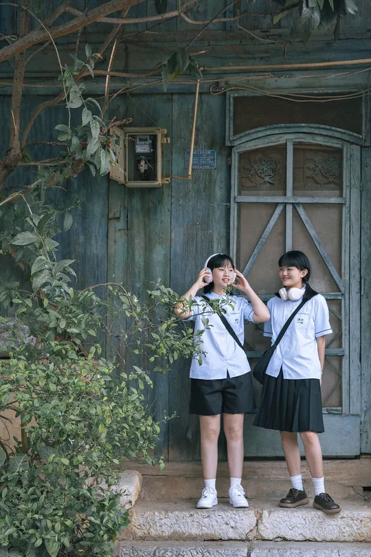 一个穿着制服的年轻男孩和女孩站在一扇房子的外面 门开着。