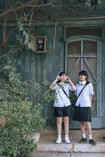 一个穿着制服的年轻男孩和女孩站在一扇房子的外面 门开着。