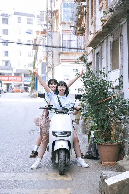 一些年轻人骑摩托车沿着一条狭窄的街道行驶 这条街道旁边有一栋建筑。