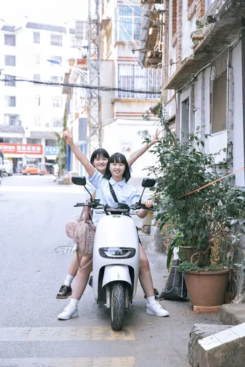 一些年轻人骑摩托车沿着一条狭窄的街道行驶 这条街道旁边有一栋建筑。