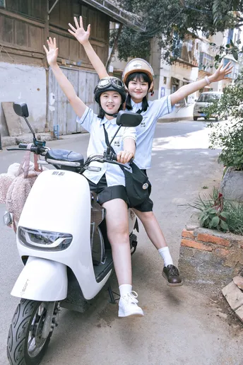 一些人在骑摩托车或滑板车 一个男孩和一个女孩 微笑着戴着头盔。