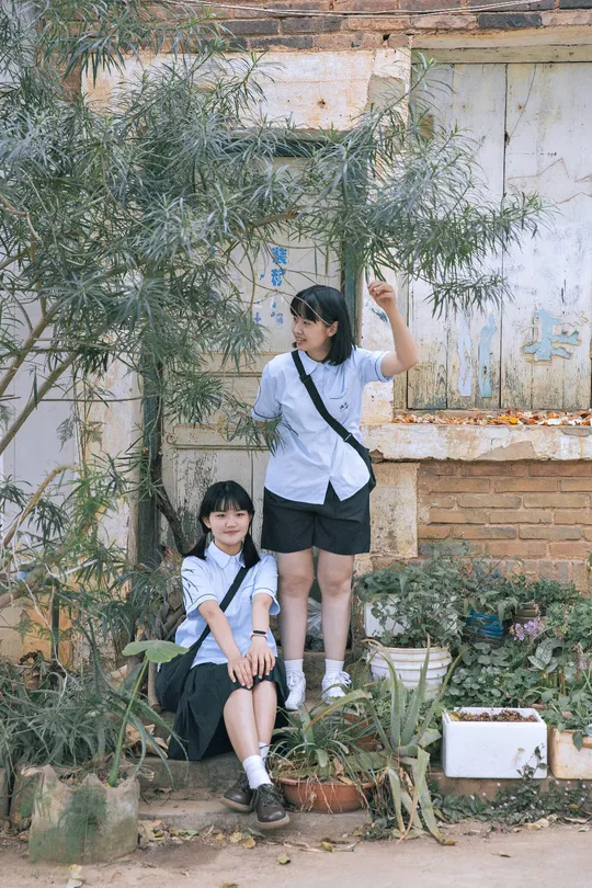 一个小男孩和一个小女孩站在一个破败的建筑前 那里有一些植物和一棵树。