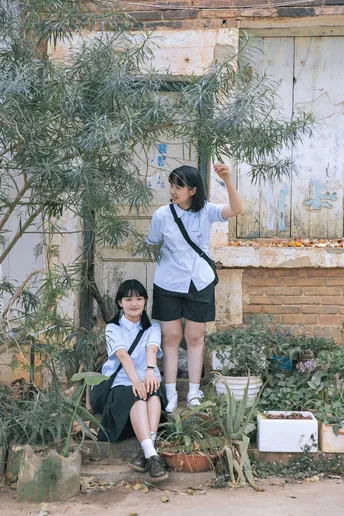 一个小男孩和一个小女孩站在一个破败的建筑前 那里有一些植物和一棵树。