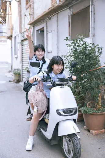 一些年轻人骑着摩托车在一条街道上 旁边有一栋建筑 一个女孩坐在摩托车上。