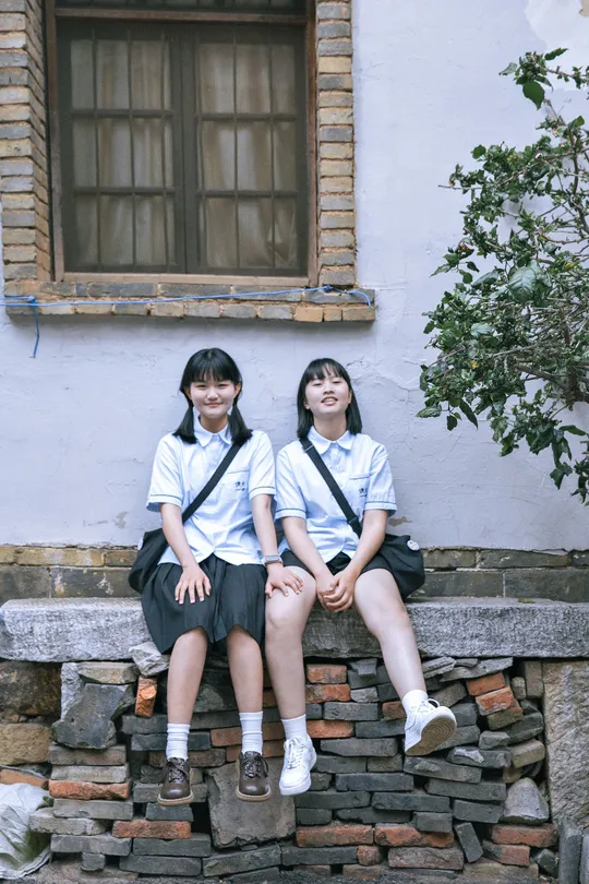 两个穿制服的女孩坐在墙前一座建筑前