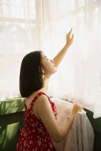 一个穿着红裙子的年轻女子坐在沙发上 凝视着窗户。
