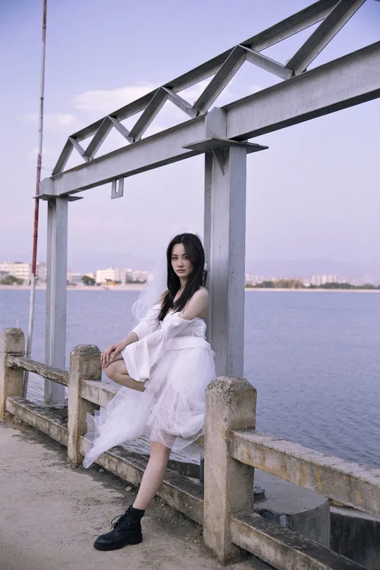 一个穿着白色连衣裙的年轻女子坐在水边的一个码头上