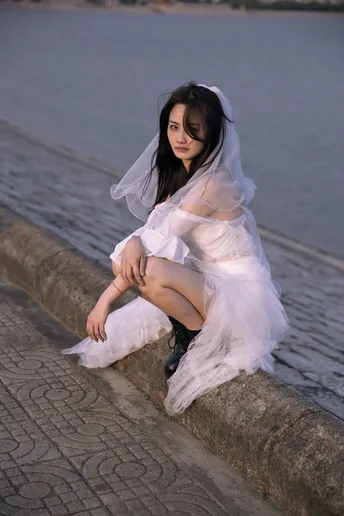 一个穿着白色连衣裙的年轻女子坐在靠近水域的墙上