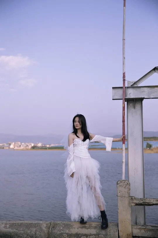 一位穿着白色连衣裙的女子在靠近水域的码头上摆姿势