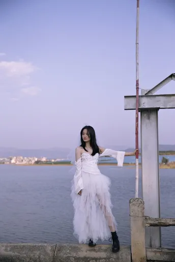 一位穿着白色连衣裙的女子在靠近水域的码头上摆姿势