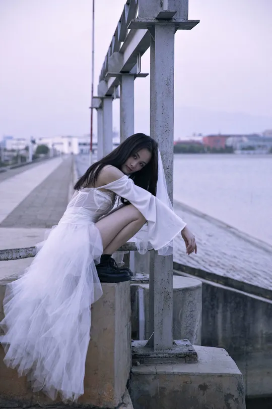 一个穿着白色裙子的美女坐在码头上