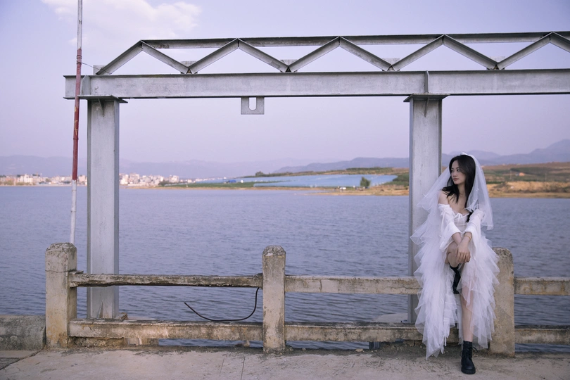 一位穿着白色连衣裙的女人坐在码头上 眺望着一片水域。