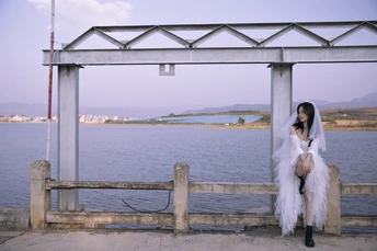 一位穿着白色连衣裙的女人坐在码头上 眺望着一片水域。