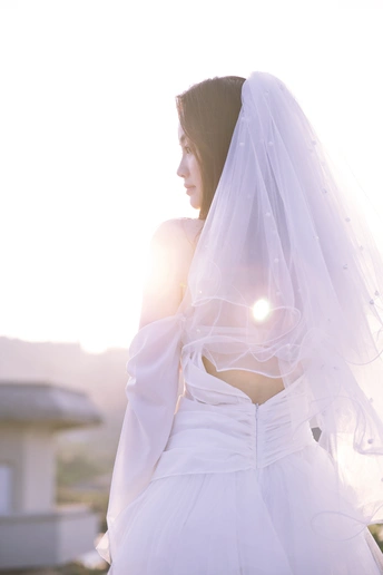 一位美丽的年轻女子穿着一件白色连衣裙和面纱站在屋顶上 太阳在她的身后。