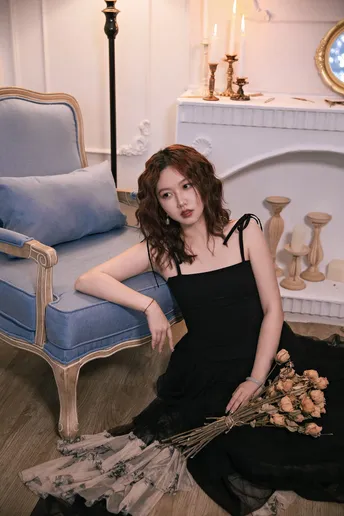 一个穿着黑色连衣裙的年轻女子坐在一个蓝色的椅子上 房间里有一个壁炉和扫帚放在地板上。