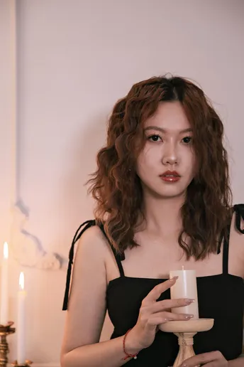 一位穿着黑色连衣裙的年轻女子手里拿着一杯和一支蜡烛。