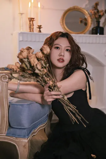 一个穿着黑色连衣裙的美丽年轻女子 手里拿着一束干玫瑰花 坐在壁炉前的一把椅子上。