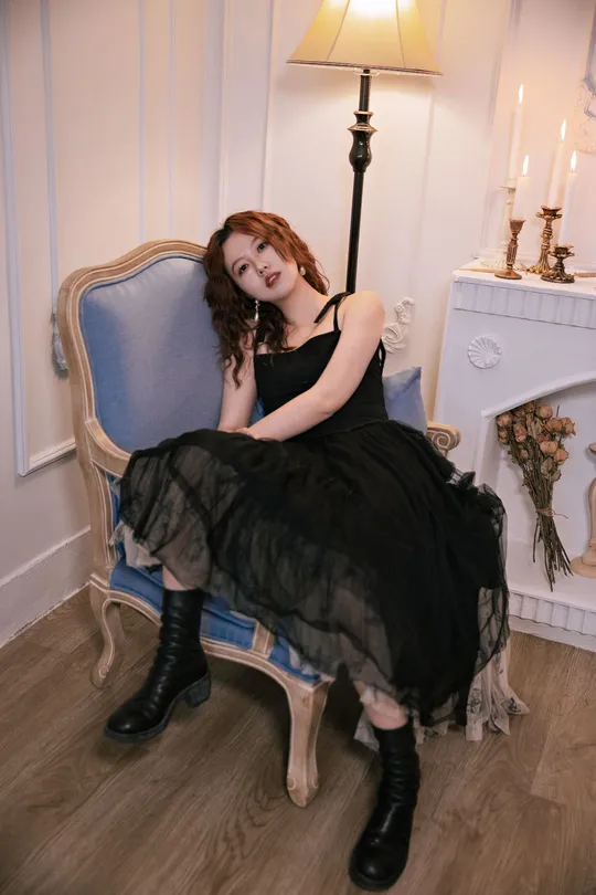 一位穿着黑色连衣裙和靴子的年轻女子坐在一个带有壁炉的蓝色椅子上。