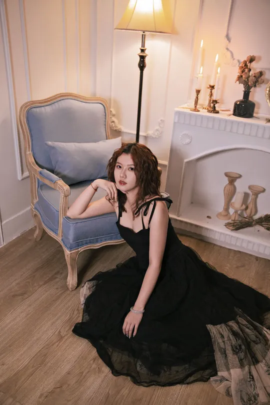 一个穿着黑色连衣裙的美丽年轻女子坐在一个带有壁炉的房间里 前面有一把蓝色的椅子。