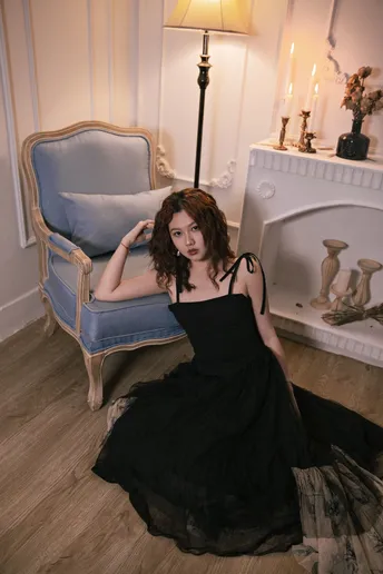 一位穿着黑色连衣裙的美丽年轻女子坐在一个带壁炉的房间里的一把蓝色椅子上。