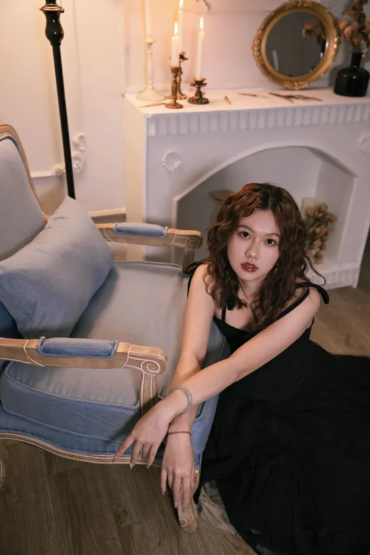 一个穿着黑色连衣裙的美丽年轻女子坐在带有壁炉的客厅里的蓝色沙发上 地板上有一把蓝色的椅子。