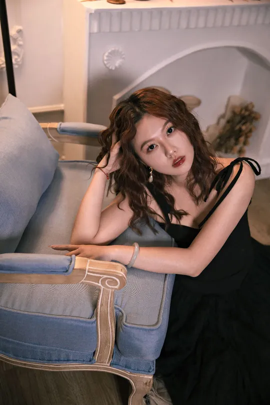 一位穿着黑色连衣裙的美丽年轻女子坐在一把蓝色的椅子上。