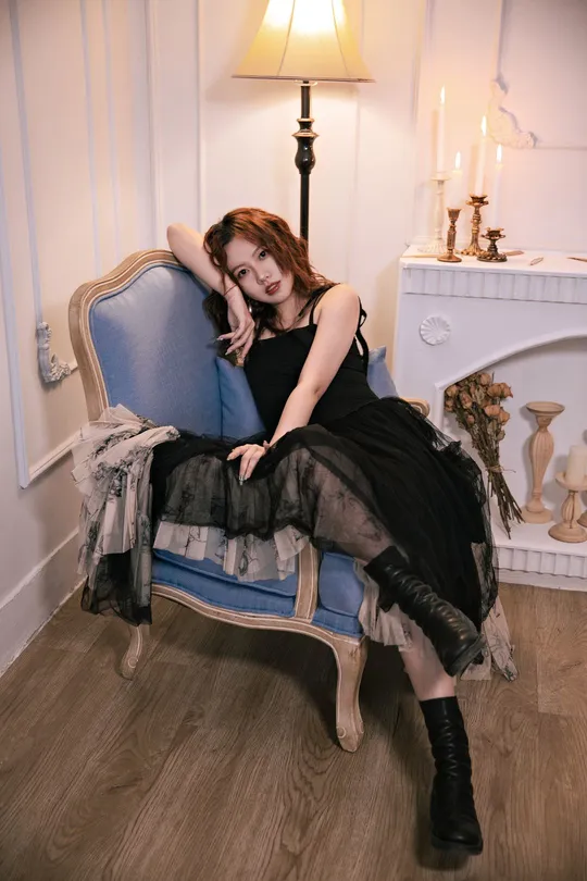 一位穿着黑色连衣裙的美丽年轻女子坐在一个蓝色椅子上 在一个白色墙壁的房间里。