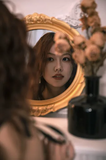 一位年轻女子将一束干花插在头上 正对着镜子