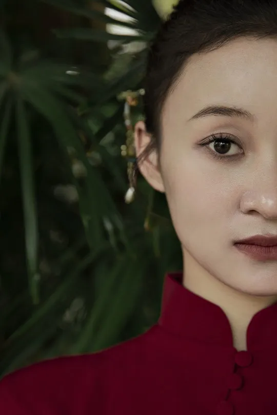 一位穿着红衬衫和耳环的女性在植物前为肖像摆姿势