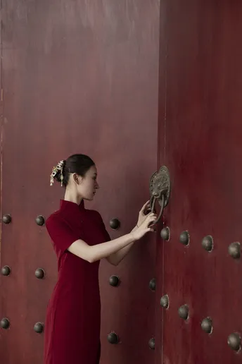 一位穿着红裙子的年轻女子站在门前 双手握住门把手。