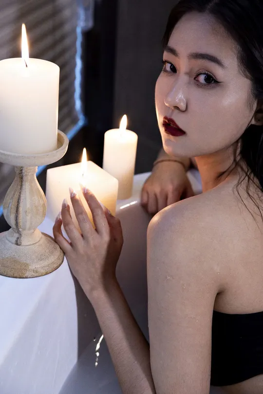 一个年轻女子坐在浴缸里 手里拿着一支点燃的蜡烛 由另一个女人点燃。